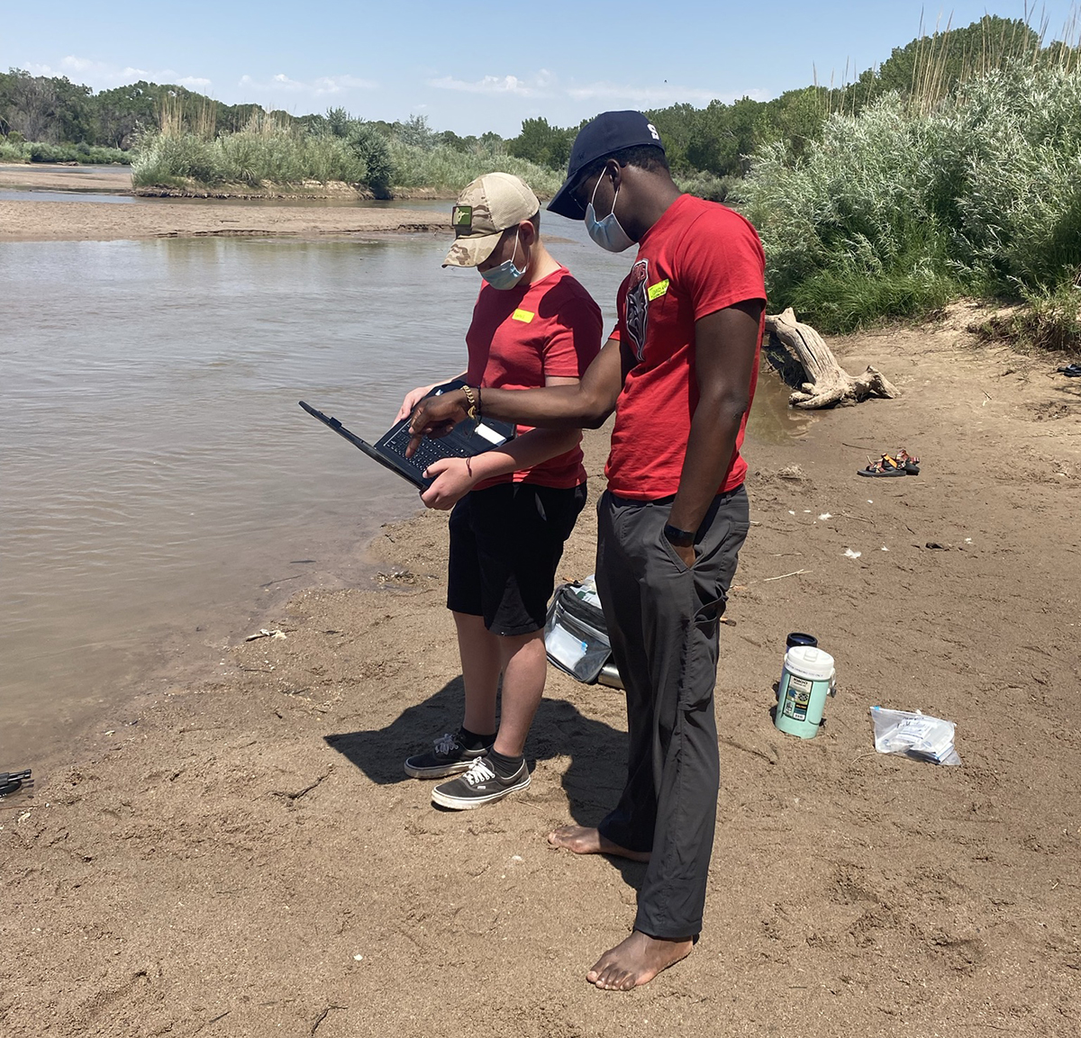 photo: 2 students on the bank of a river with laptop